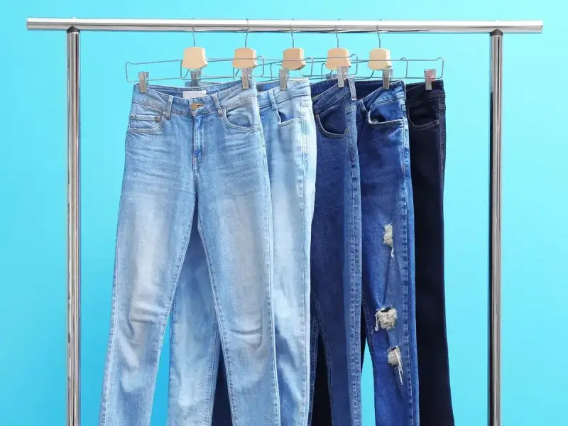 Różne modele jeansów na wieszakach. Czy rozmiar 27 spodnie damskie to Twój idealny rozmiar?